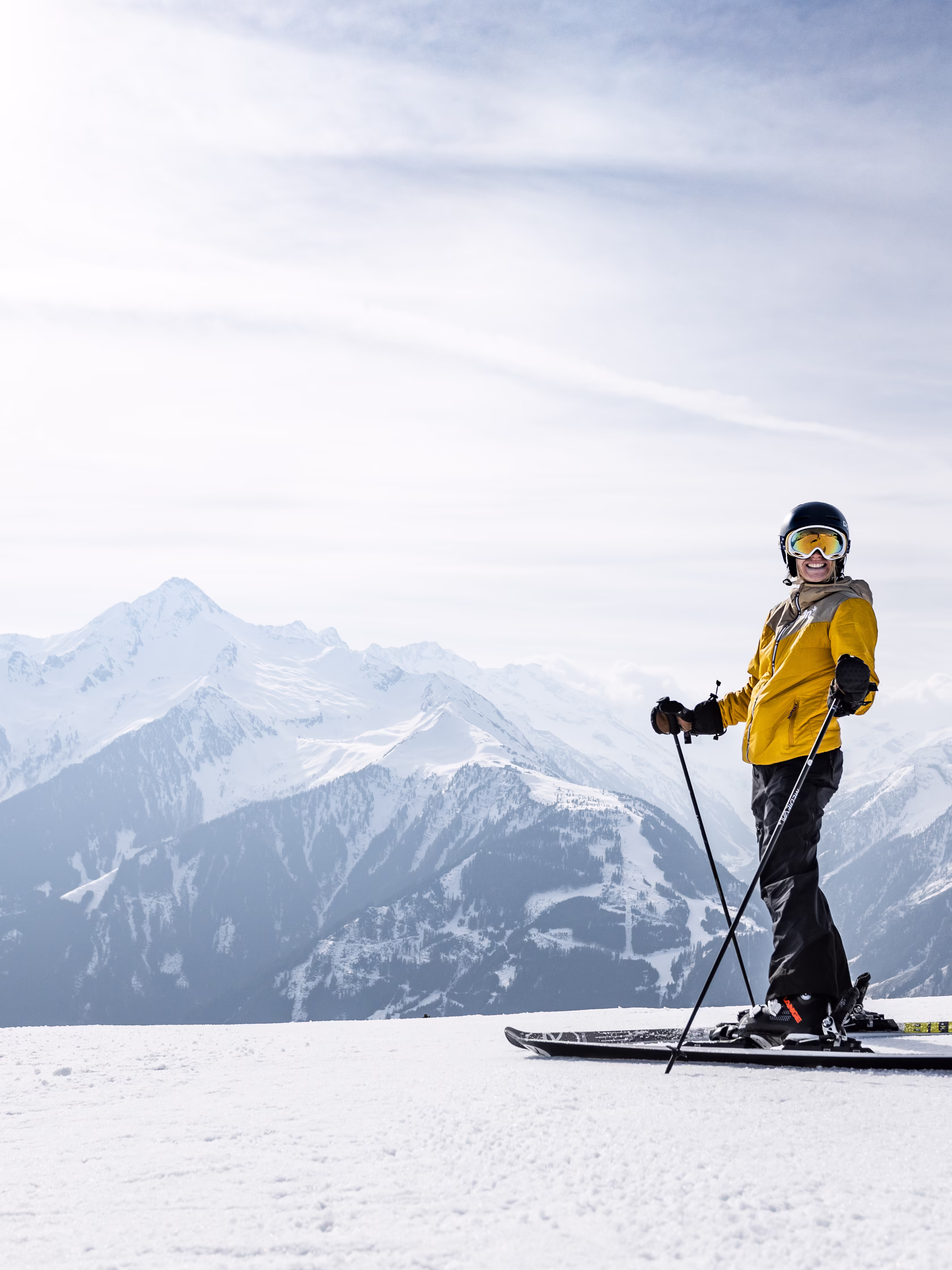 Skifahrerin steht mit Ausrüstung und gelber Jacke auf der Piste